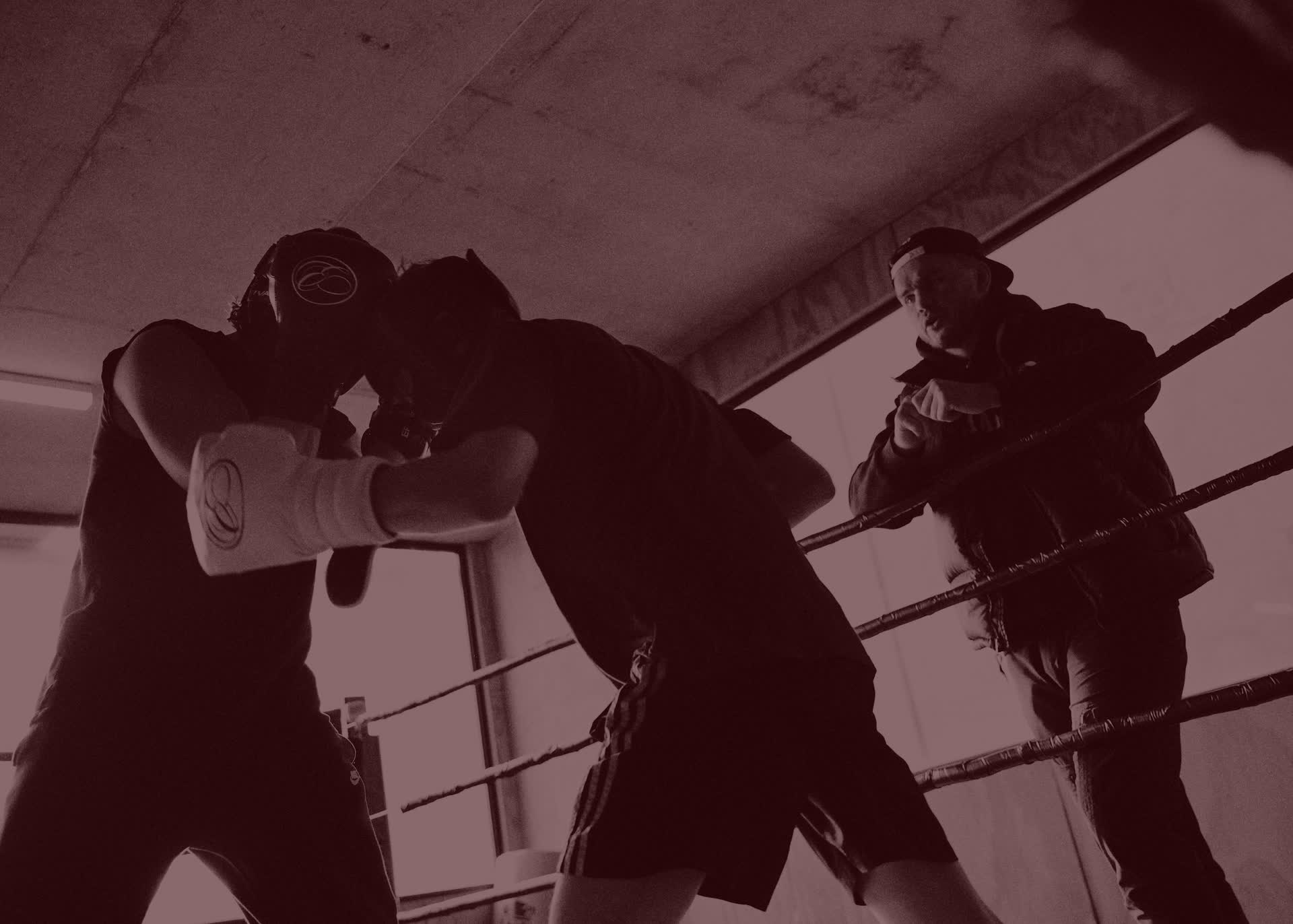 Two boxers sparring in the ring while a coach watches from the ropes